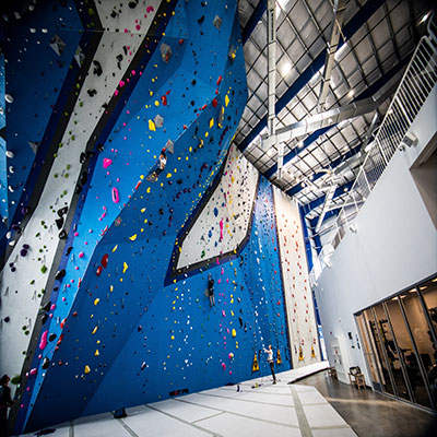 Blue and gray rock climbing wall with student climbing and instructor belaying