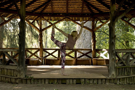yoga instructor in pose in gazebo with trees and greenery in background