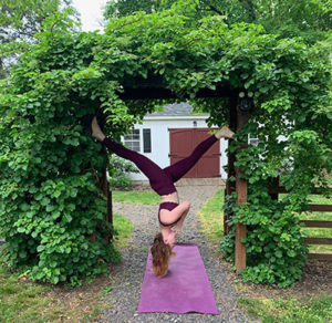 yoga instructor in upside down pose between arch with greenery