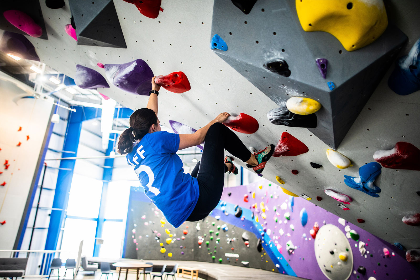 instructor bouldering on gray wall with colorful grips