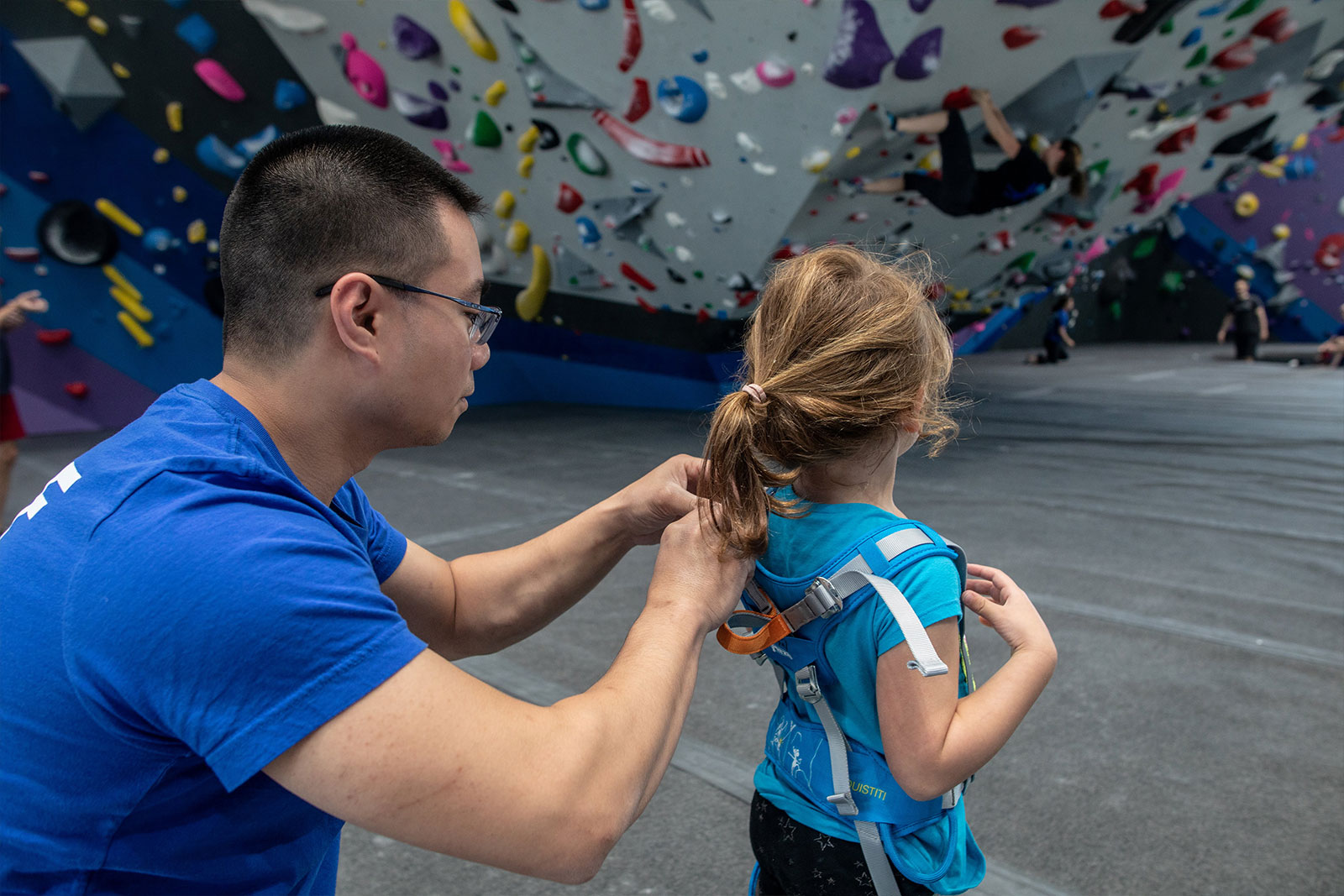 instructor putting harness on child with rock climbing wall in background